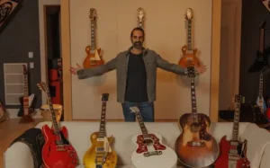 El argentino César Gueikian, Asesor Estratégico de Gibson Guitars, posando con los brazos abiertos frente a una colección de guitarras de la marca junto a Green Glass.