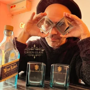 El artista Lanchi de Green Glass en una pose creativa con bases de botellas Blue Label como anteojos de vidrio reciclado.
